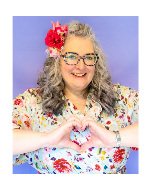 Vie in a floral dress, flowers in hair creating a heart shape with her hands.
