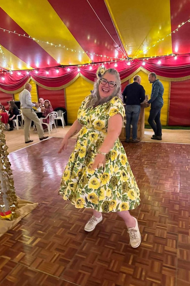 A woman in a bright floral dress dances joyfully under a festive tent.